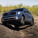 Blue 2023 Kia Telluride SX X-Pro on an off-road course, with its left front wheel in the air as it crawls out of a ditch.